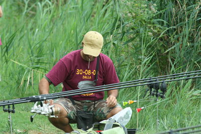 Man cleaning fishing rod while crouching on field