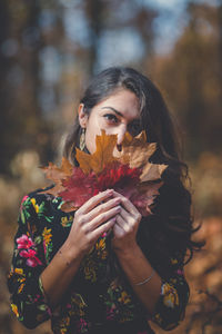 Portrait of young woman holding maple leaves during autumn