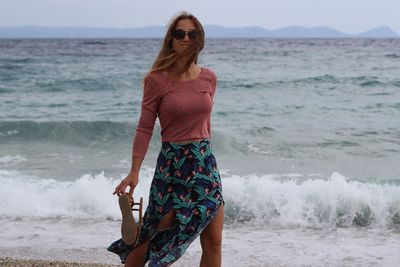 Young woman standing at beach against sky