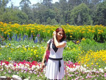 Beautiful young woman standing by yellow flowers on field