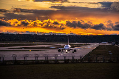 Airplane on runway against sky during sunset