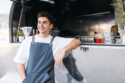 Smiling young chef looking away while standing by food truck