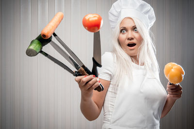 Young woman holding vegetables with knives while standing in kitchen