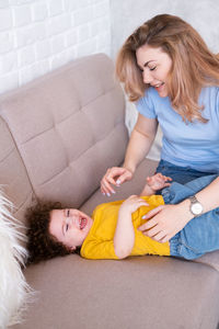 Mother tickling son on sofa at home