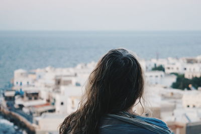 Rear view of woman standing against sea and cityscape