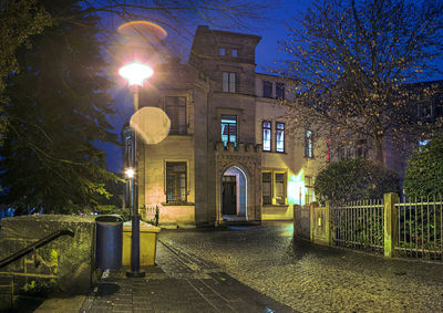 Illuminated street light by building against sky at night