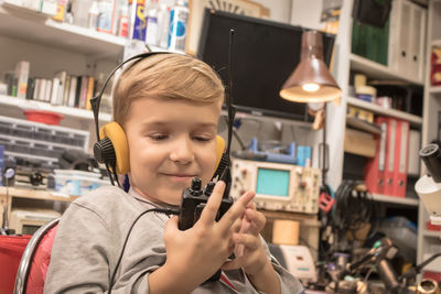 Smiling boy holding walkie-talkie while sitting in workshop