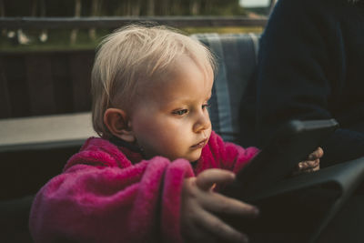 Close-up of girl holding digital tablet while sitting by mother