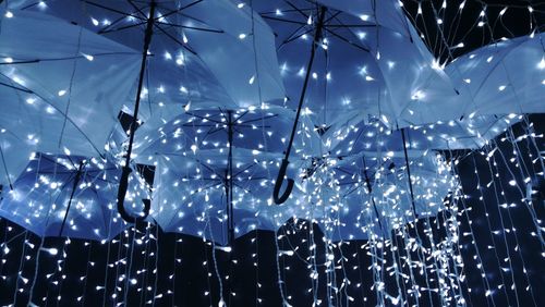 Low angle view of illuminated string lights and umbrellas at night