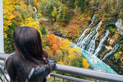 Rear view of woman standing by railing during autumn