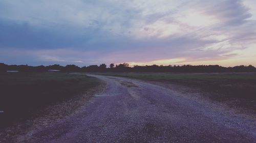 Road passing through field against cloudy sky