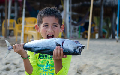 Boy holding fish while standing at beach