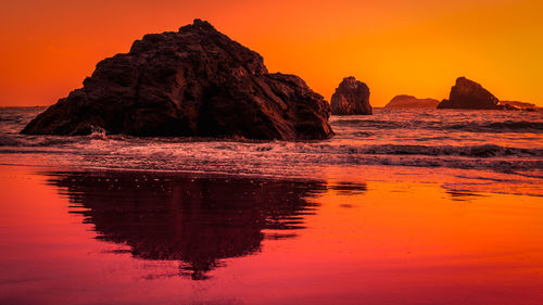 Rock formations in sea against orange sky