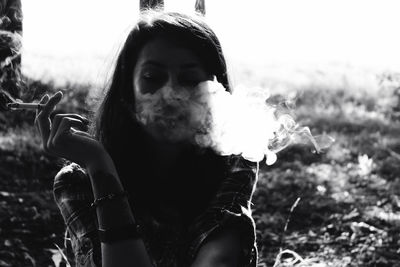 Woman smoking cigarette while sitting against trees