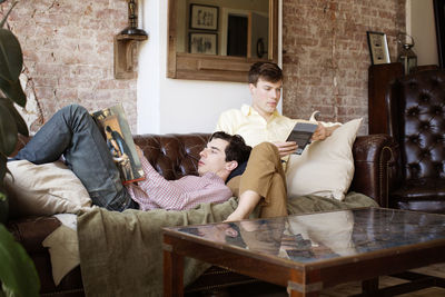 Gay couple reading books while relaxing on sofa at home