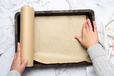 Two female hands cover with brown parchment paper an iron rectangular baking sheet, top view