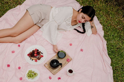 High angle view of woman having drink while lying on picnic blanket in yard