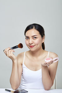 Portrait of beautiful mid adult woman applying make-up over gray background
