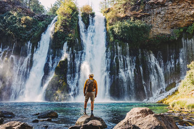 Rear view of woman standing against waterfall