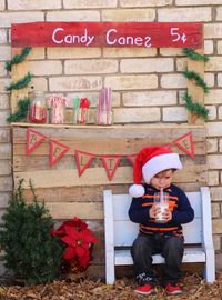 Full length of boy with santa hat sitting on bench against wall during christmas