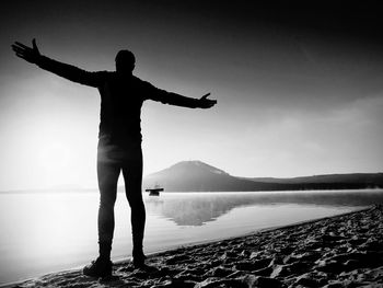 Rear view of silhouette man standing by lake against sky