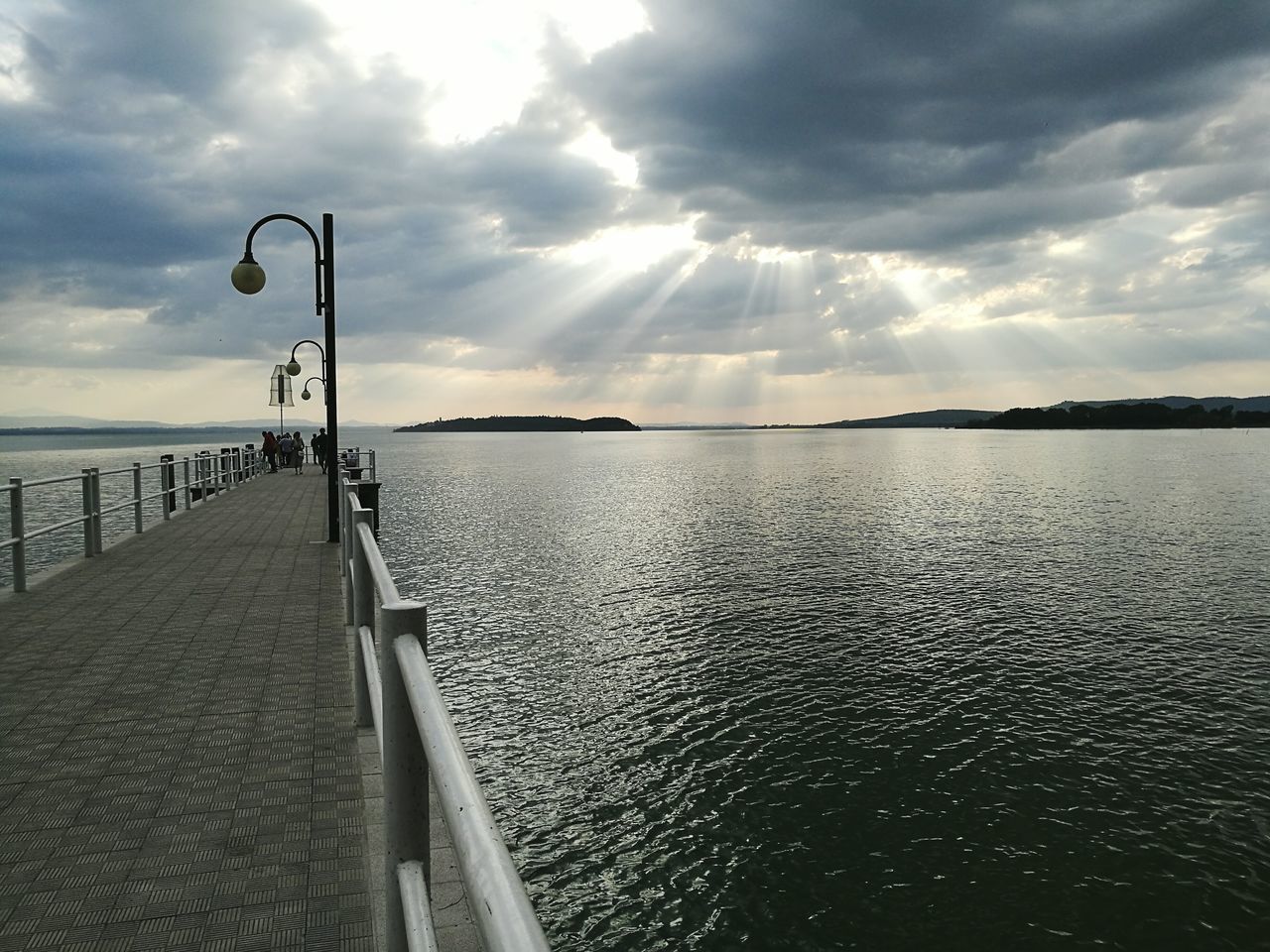 water, street light, calm, sea, tranquil scene, the way forward, lake, tranquility, ocean, pier, cloud, sky, in a row, scenics, walkway, rippled, diminishing perspective, cloud - sky, idyllic, narrow, railing, day, solitude, long, lamp post, pathway, sunbeam, jetty, remote, nature, non-urban scene, beauty in nature, vanishing point