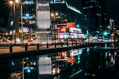 Illuminated buildings by river in city at night