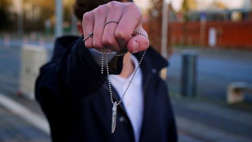 Close-up of man holding dog tag while standing on street