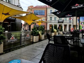 Empty chairs and tables in street amidst buildings in city