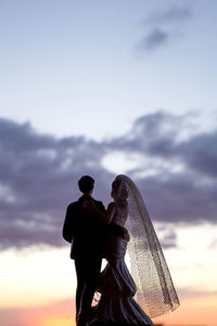 Couple figurines against sky during sunset