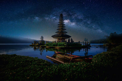 Traditional windmill by lake against sky at night