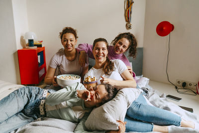 Happy female friends watching tv while enjoying snacks at home