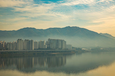 View of city at waterfront against cloudy sky