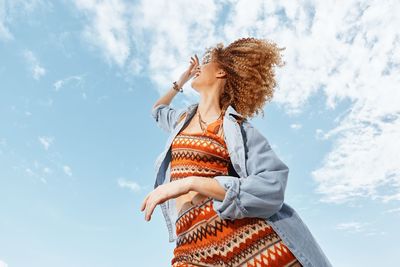 Low angle view of young woman standing against sky