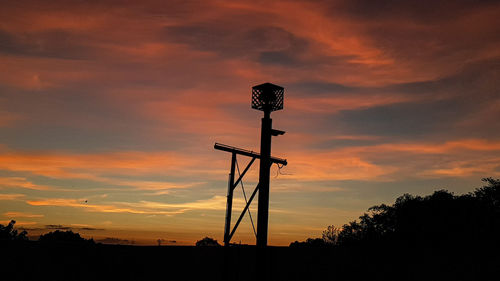 Low angle view of silhouette communications tower on field against sky during sunset