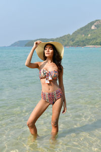 Full length of beautiful woman standing at beach against sky