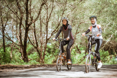 Full length of young females riding bicycles on road