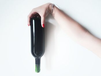 Cropped hand of woman holding wine bottle against white background