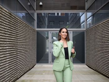 Portrait of young woman standing against building