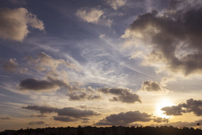 Low angle view of sunlight streaming through clouds during sunset