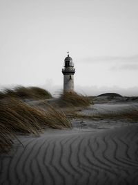 Lighthouse at beach against sky