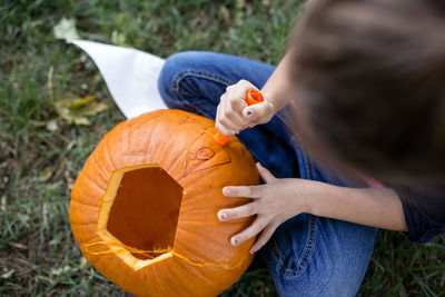 High angle view of girl carving pumpkin while sitting on field in yard during halloween