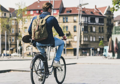 Young man holding skateboard riding bicycle in the city