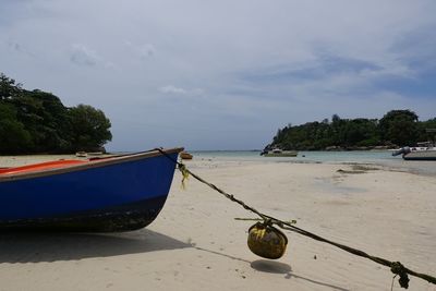 Boat moored on beach against sky