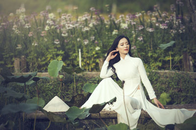 Smiling young woman standing by plants against trees