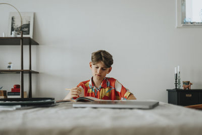 Boy doing homework while sitting near table at home