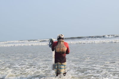 Rear view of man standing on beach against clear sky