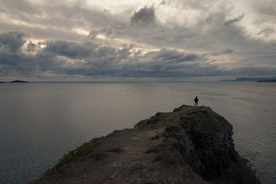 Distant view of man looking at sea while standing at cliff