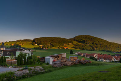 Houses on field by buildings against clear sky