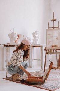 Side view of young woman using mobile phone while standing against wall